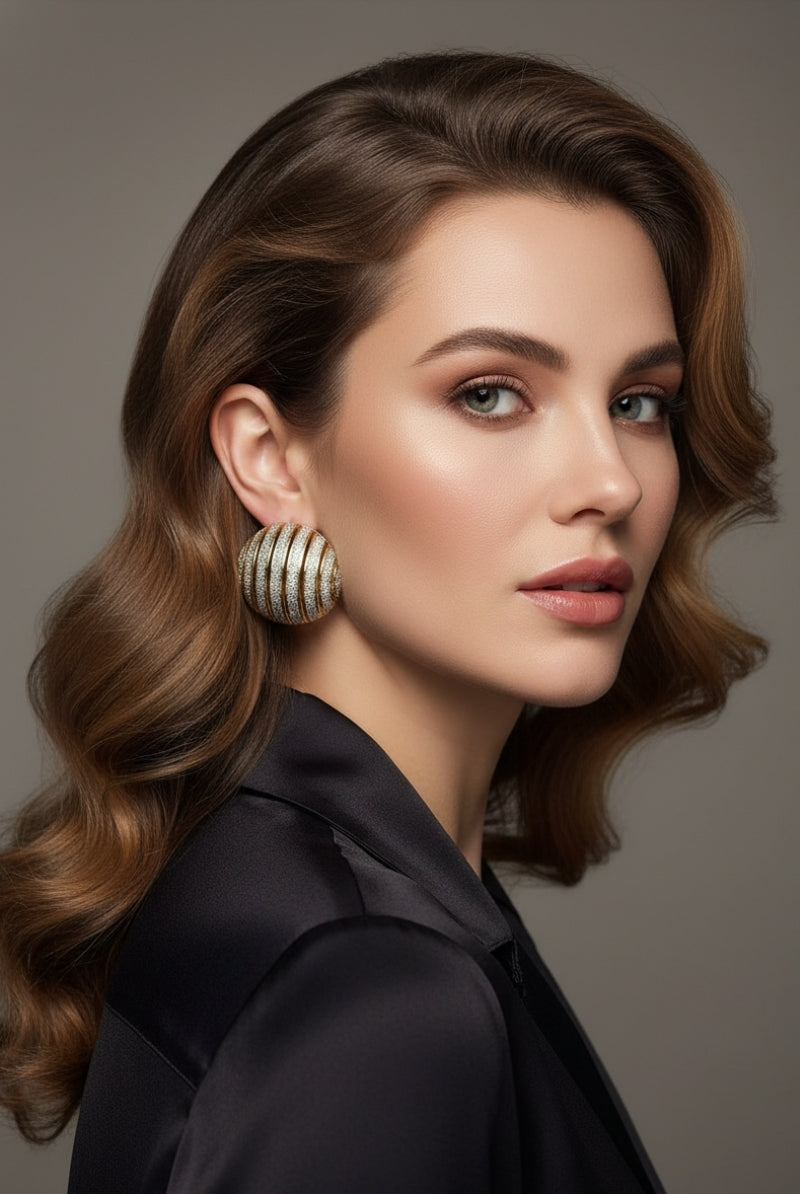 A model wearing off-the-shoulder black top paired with large ribbed dôme earrings, featuring a two-tone gold and diamond-dust textured effect.