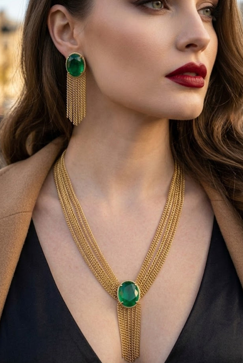 Close-up of a luxury emerald green Eclipse jewelry set featuring a gold multi-strand tassel necklace and matching fringe earrings on a model, styled for a sophisticated evening out in Paris or a red carpet event in Los Angeles.