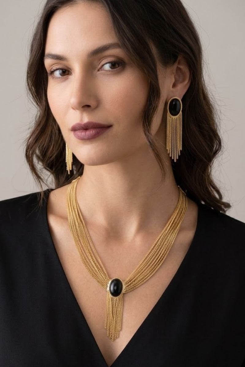 A vintage gold multi-chain necklace and matching long tassel earring set with black oval stones and mesh fringes, suitable for formal wear in fashionable global cities like New York and Paris, presented as a professional studio shot on a clean white background.