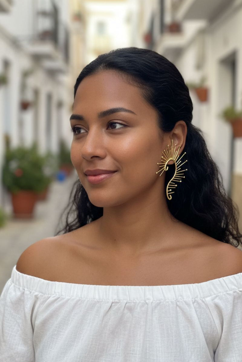 Smiling model wearing maximalist gold sunburst ear crawlers in a bright Mediterranean street setting. Versatile statement earrings for summer vacations and resort wear.