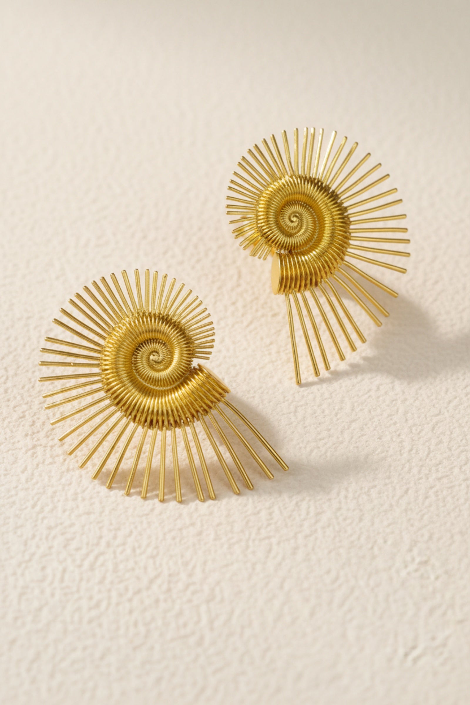 Large golden spiral wire earrings with a nautilus-inspired geometric design, showcasing the oversized architectural silhouette.