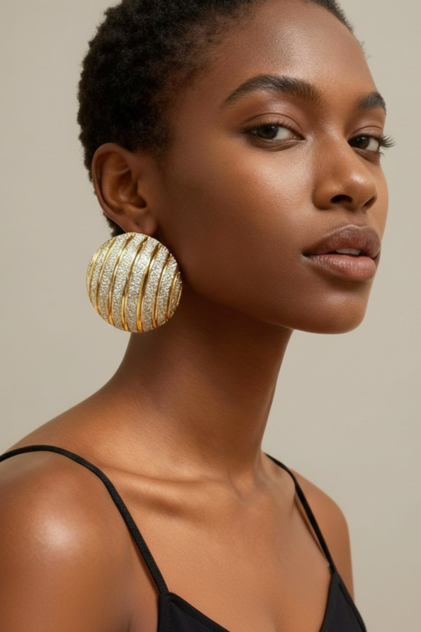Woman wearing oversized ribbed gold dome earrings for a mob wife aesthetic look.