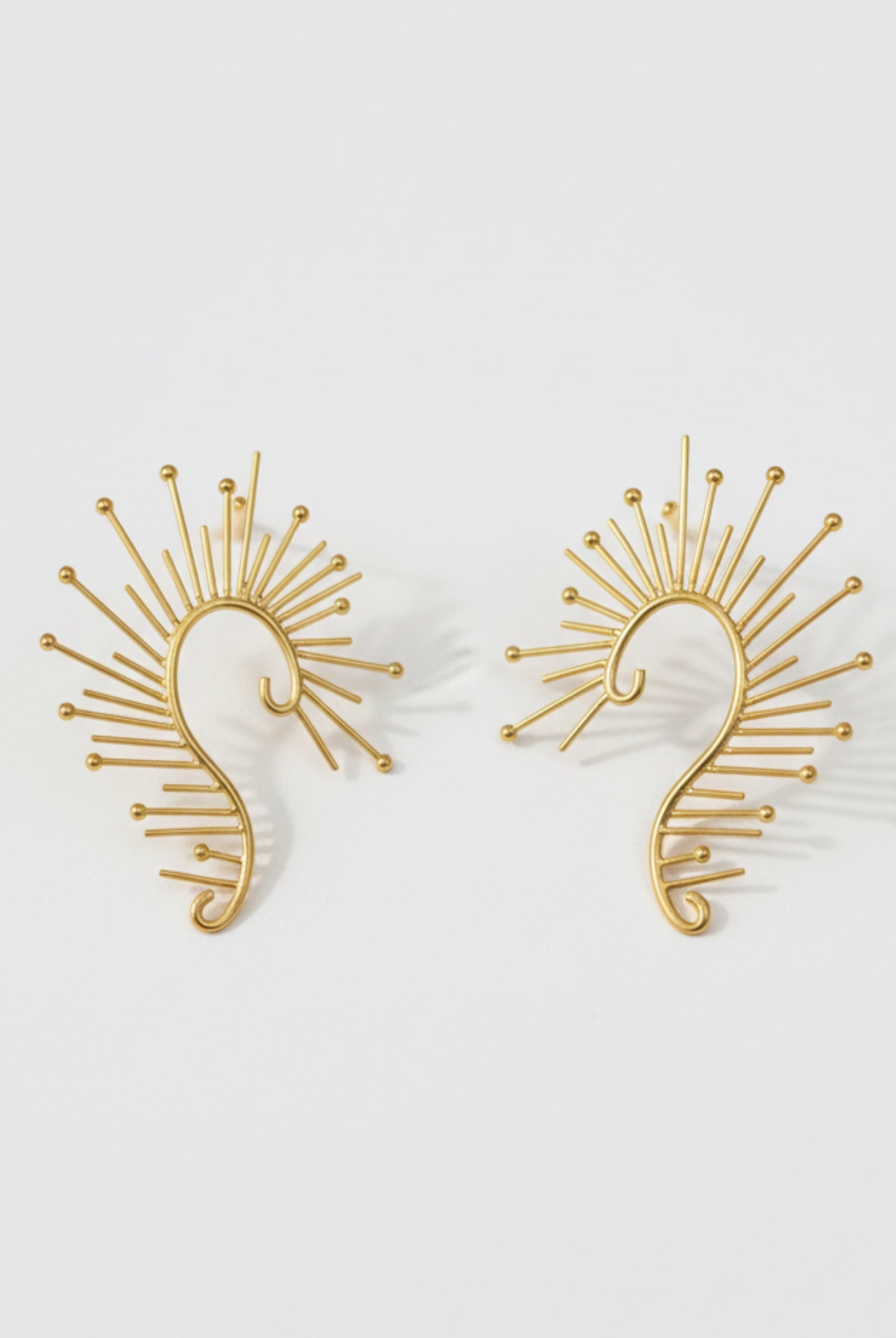 Large golden spiral wire earrings with a nautilus-inspired geometric design, showcasing the oversized architectural silhouette.