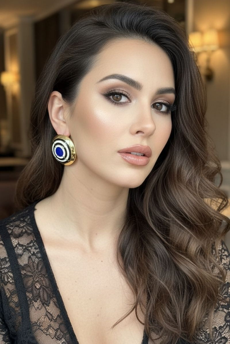 Close-up portrait of a model wearing All-Glows Grand Muse cobalt blue enamel earrings with a gold border. Vintage-inspired statement jewelry that provides a high-fashion editorial look.