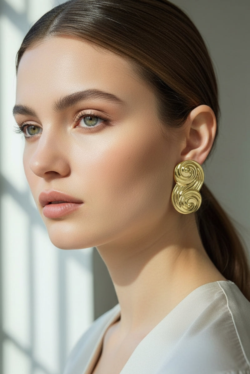 Side profile of a model with a sleek bun wearing gold sculptural swirl studs, a top trend for New York fashion week.