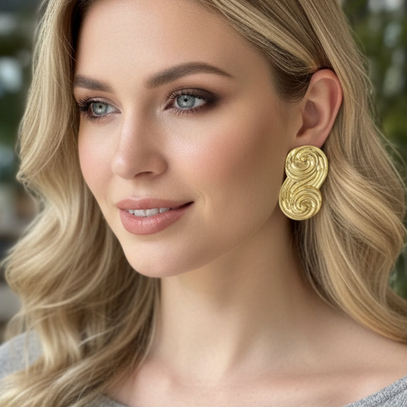 Model wearing gold Seraphina sculptural swirl stud earrings with grey knitwear
