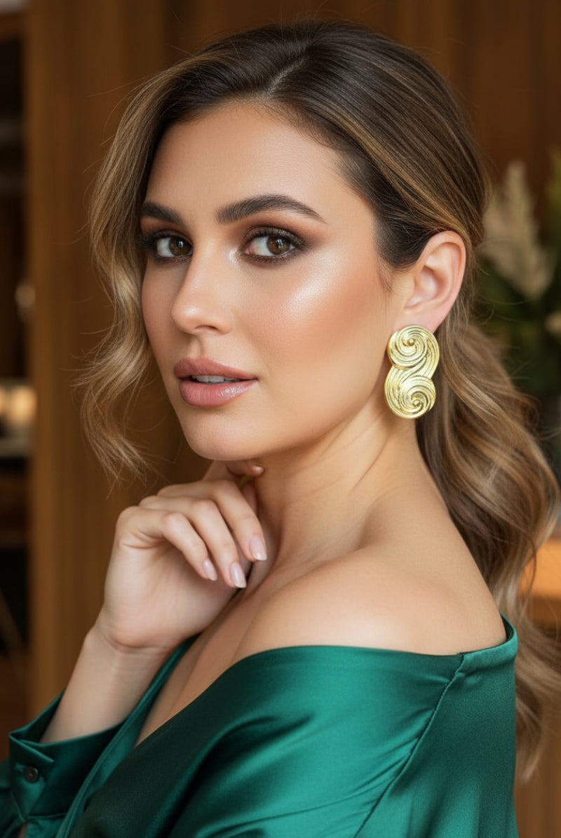 Bold gold infinity stud earrings paired with an emerald green silk dress, luxury statement jewelry for evening events.