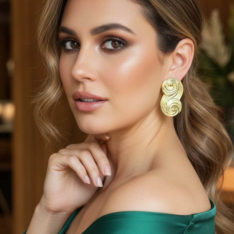 Bold gold infinity stud earrings paired with an emerald green silk dress, luxury statement jewelry for evening events.
