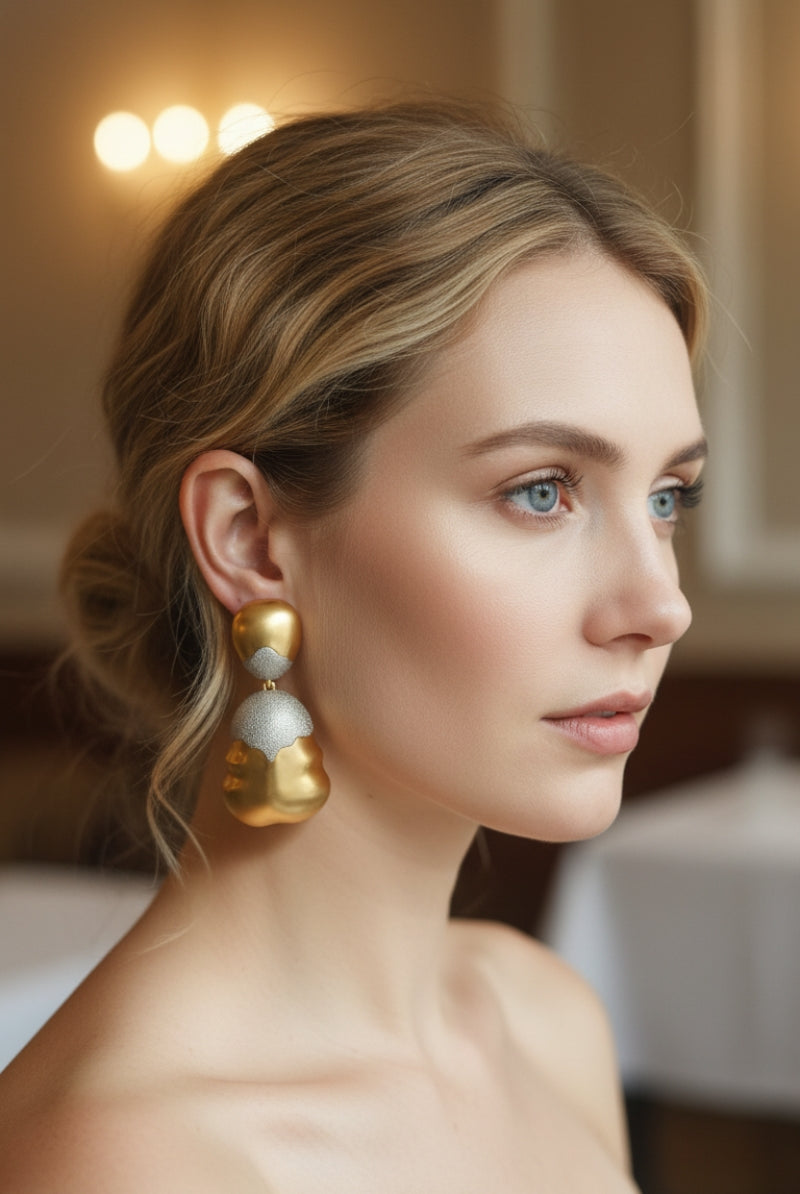Modern woman wearing chunky sculptural two-tone earrings in gold and silver, featuring a unique wavy organic texture and shimmering finish.