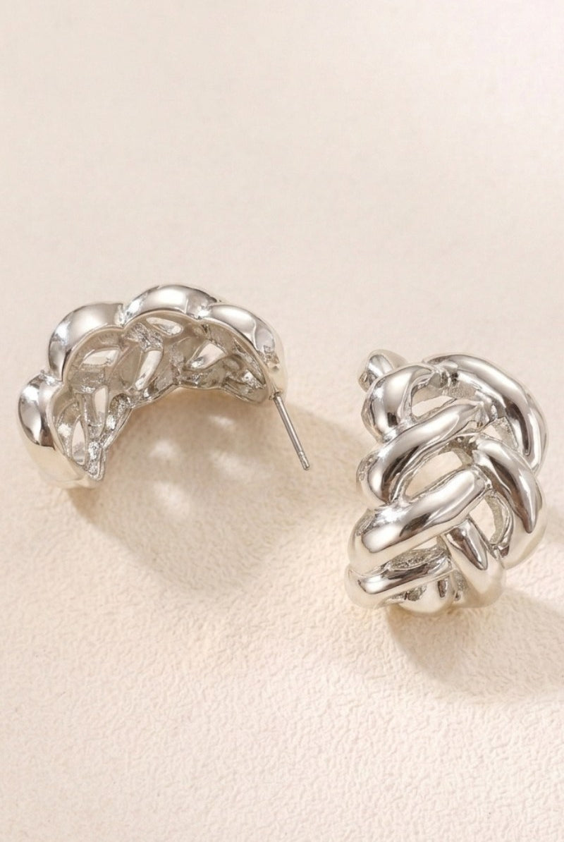 Braided liquid silver half-hoop earrings on a textured beige background