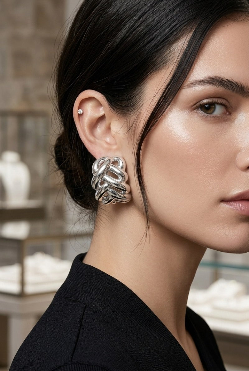 Close-up of white-gold-plated braided half-hoop earrings showing their open sculptural design