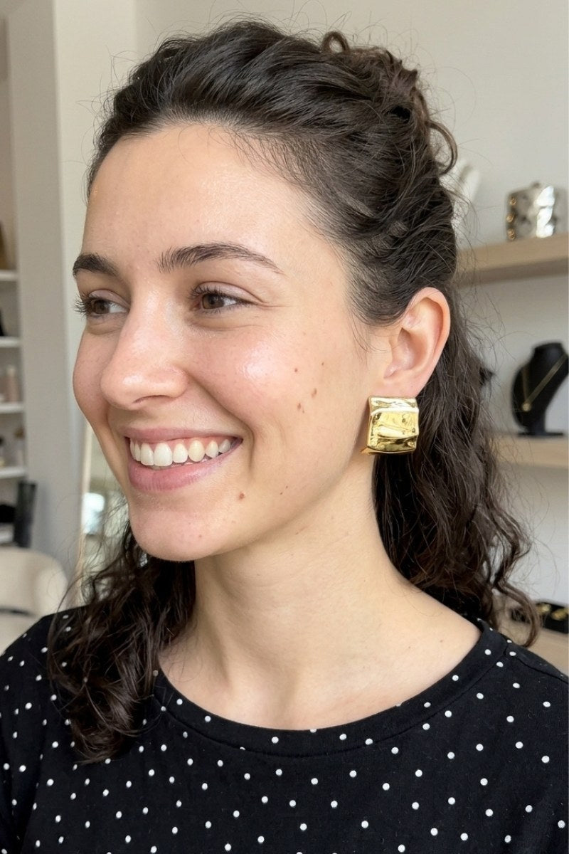 Model wearing crinkled gold square statement studs, view 1