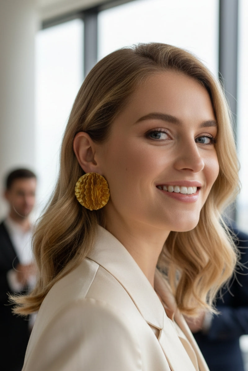 Woman wearing oversized gold honeycomb textured disc earrings in a modern office party setting.