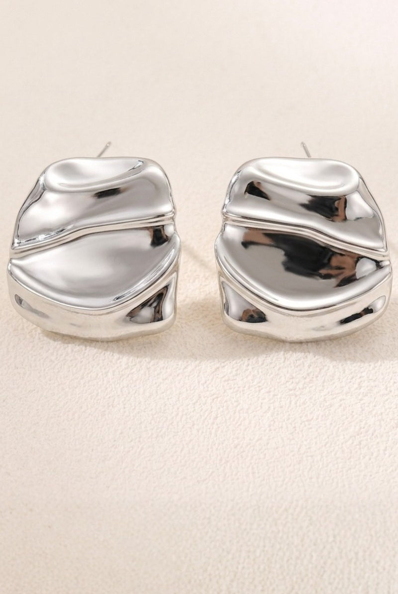 Liquid silver square statement stud earrings on a warm beige background