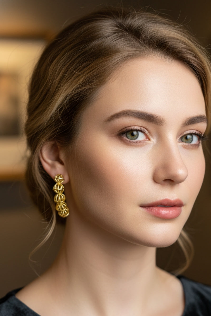 An elegant portrait of a woman with an classic updo wearing a black off-the-shoulder velvet dress, accessorized with luxury gold curved drop earrings that draw focus to her jawline for cocktail attire inspiration.