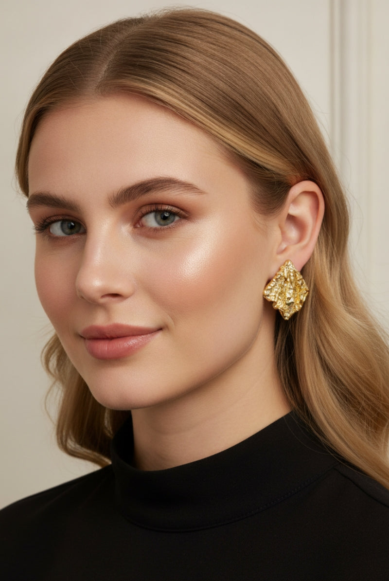 A professional lookbook photo of the Mirage Earrings, showcasing the intricate artisanal texture of the gold statement piece.