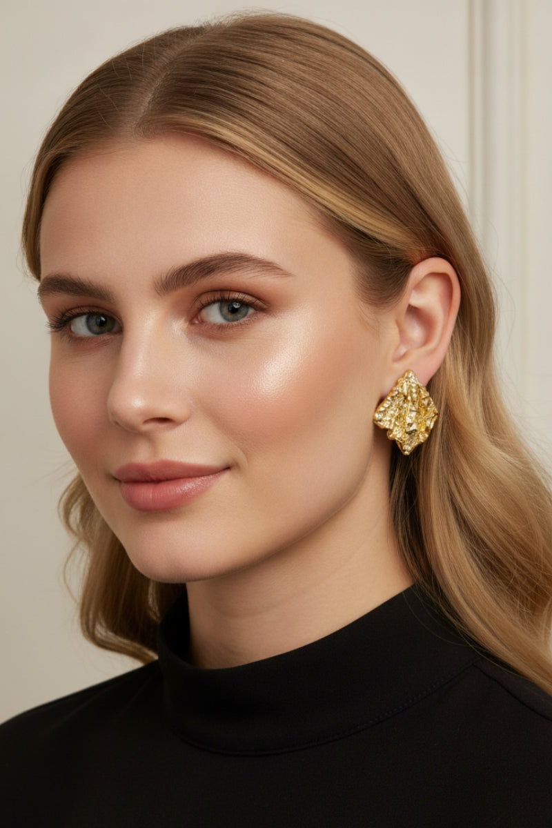 A professional lookbook photo of the Mirage Earrings, showcasing the intricate artisanal texture of the gold statement piece.