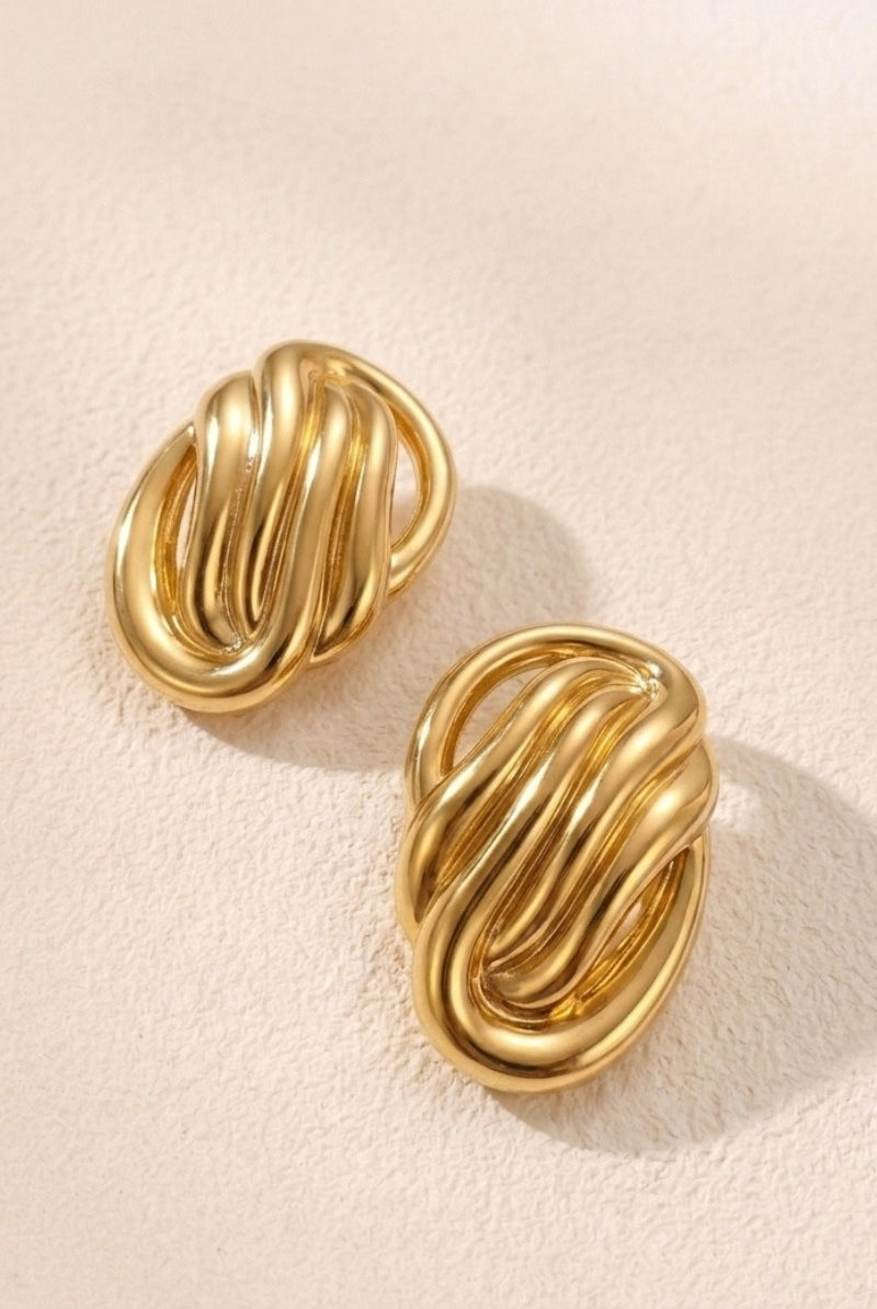 Sculptural oval knot statement stud earrings on a warm beige background