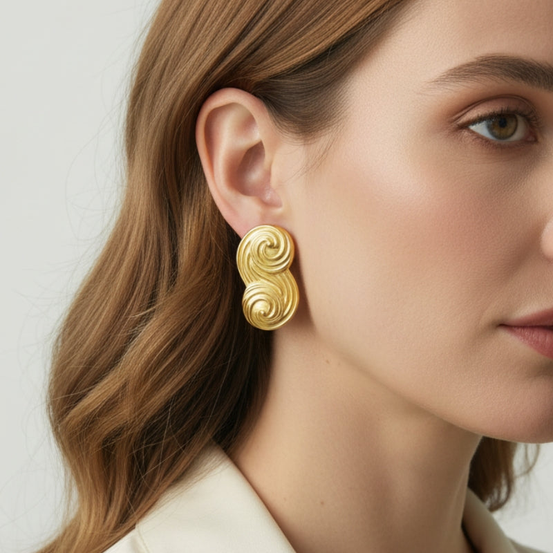 Close-up of a model wearing the Seraphina small gold S-wave stud earring, highlighting its flowing liquid-metal texture.