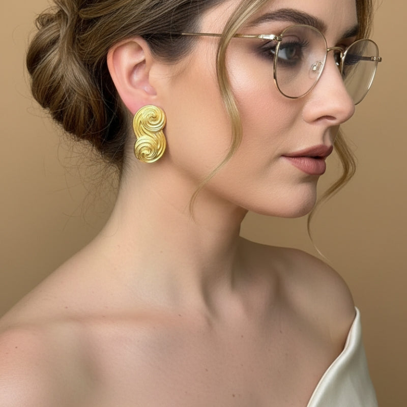 A chic lifestyle shot of a model wearing Seraphina small gold statement studs with glasses, perfect for a modern office look.