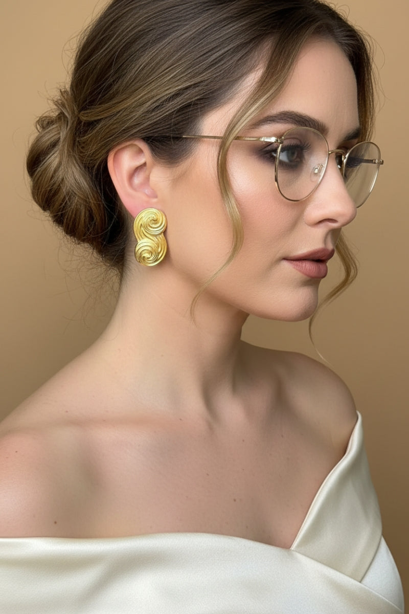 A chic lifestyle shot of a model wearing Seraphina small gold statement studs with glasses, perfect for a modern office look.