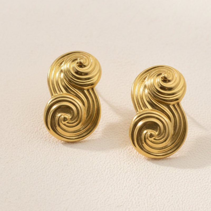 A pair of Seraphina small textured gold S-shape earrings on a neutral background, focusing on the intricate sand-cast finish.