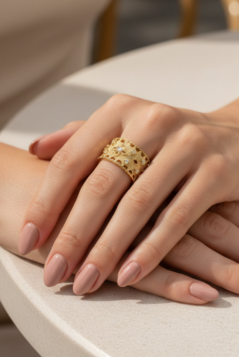 Hands clasped over a sunlit table, highlighting the sustainable luxury appeal of All Glows tarnish-resistant brushed gold filigree Ash ring.