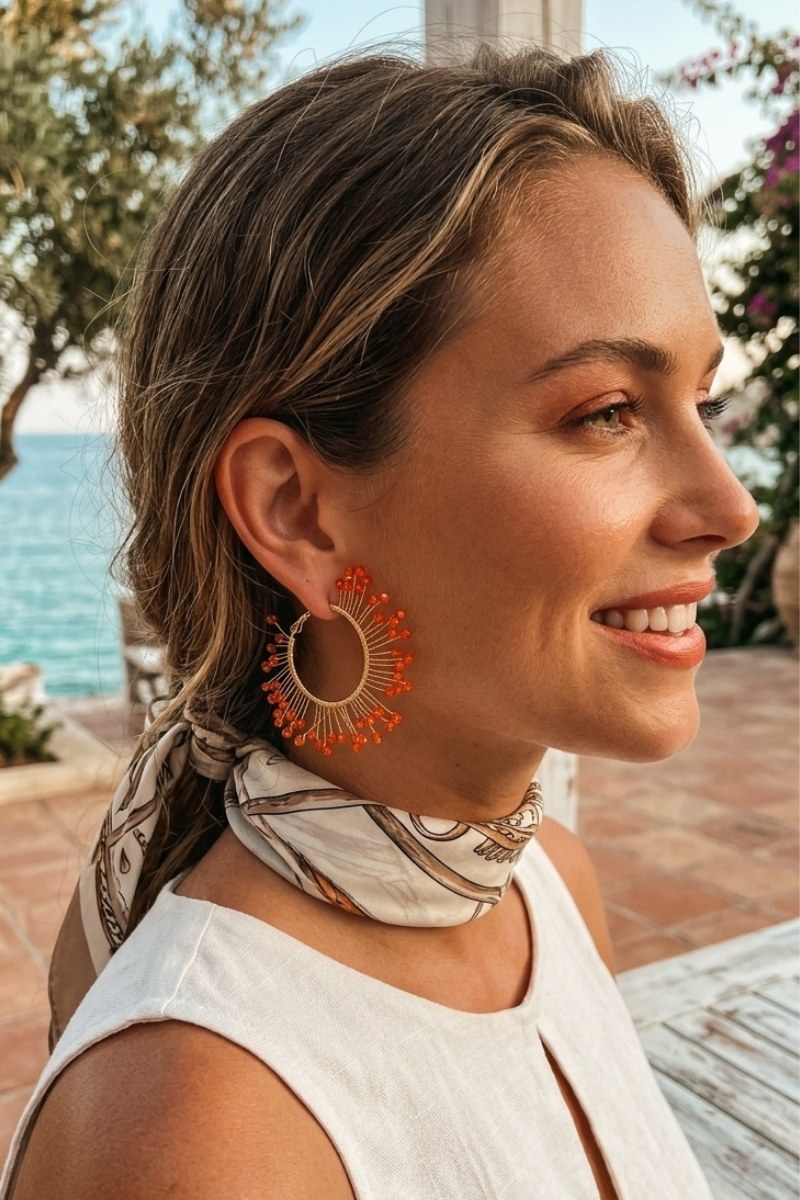 Model wearing solburst wire-wrapped beaded sunburst hoop earrings in the Tangerine variant, view 3