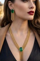 Close-up of a luxury emerald green Eclipse jewelry set featuring a gold multi-strand tassel necklace and matching fringe earrings on a model, styled for a sophisticated evening out in Paris or a red carpet event in Los Angeles.