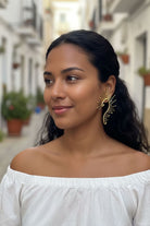Smiling model wearing maximalist gold sunburst ear crawlers in a bright Mediterranean street setting. Versatile statement earrings for summer vacations and resort wear.