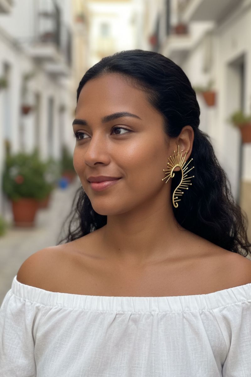 Smiling model wearing maximalist gold sunburst ear crawlers in a bright Mediterranean street setting. Versatile statement earrings for summer vacations and resort wear.