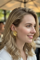 Side profile of a model wearing All-Glows Nautilus Spiral earrings in 18K gold plating. These architectural statement earrings are paired with a white linen shirt, demonstrating a sophisticated resort wear or corporate chic style.