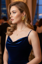 A model in a navy blue satin evening gown accessorized with All-Glows Nautilus Spiral statement studs. These architectural earrings offer a secure fit and high-polish finish for gala events and luxury weddings.