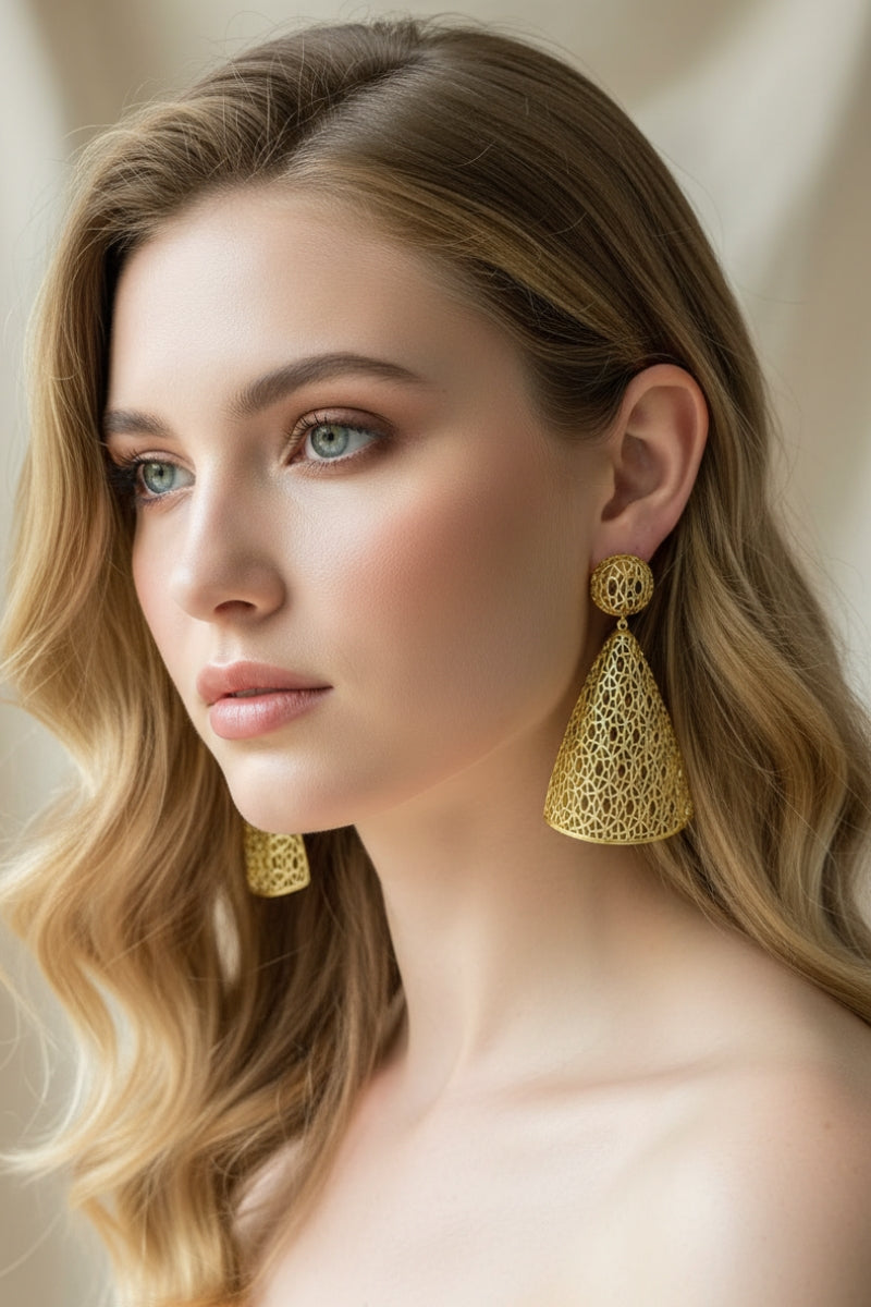 Three-quarter portrait of a model with wavy blonde hair and a strapless neck wearing intricate, conical All Glows gold plated brass lattice drop earrings.