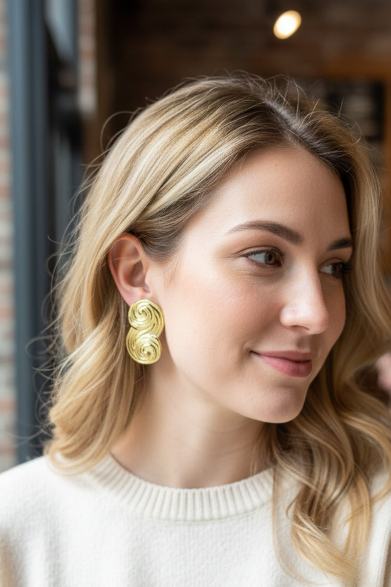 Seraphina Sculptural Swirl Earrings in gold on a woman wearing a white sweater, elegant daily style jewelry.