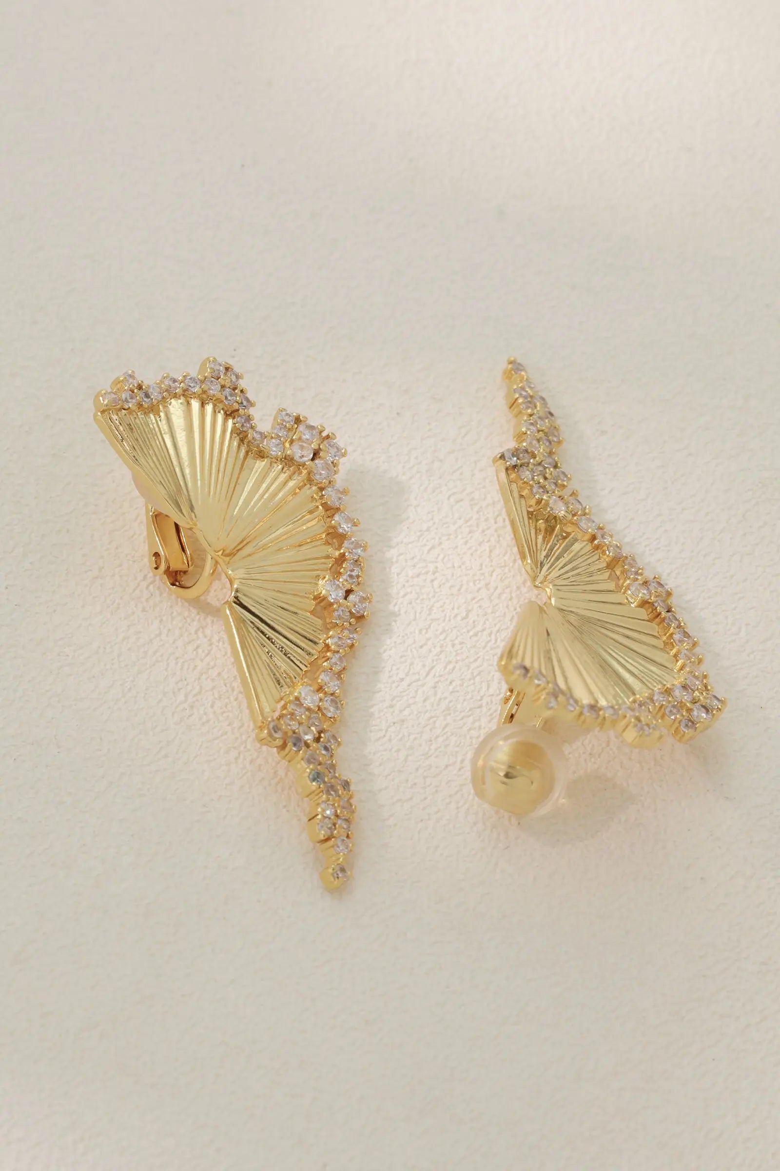 A pair of Chrysalis gold pleated earrings placed side-by-side to reveal a breathtaking sculptural butterfly silhouette with shimmering cubic zirconia borders.