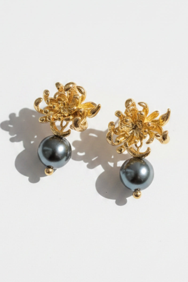 Studio flat lay of baroque style textured gold flower earrings cascading into smooth grey black pearls, casting sharp aesthetic shadows to showcase the lightweight, non-tarnishing botanical metalwork.