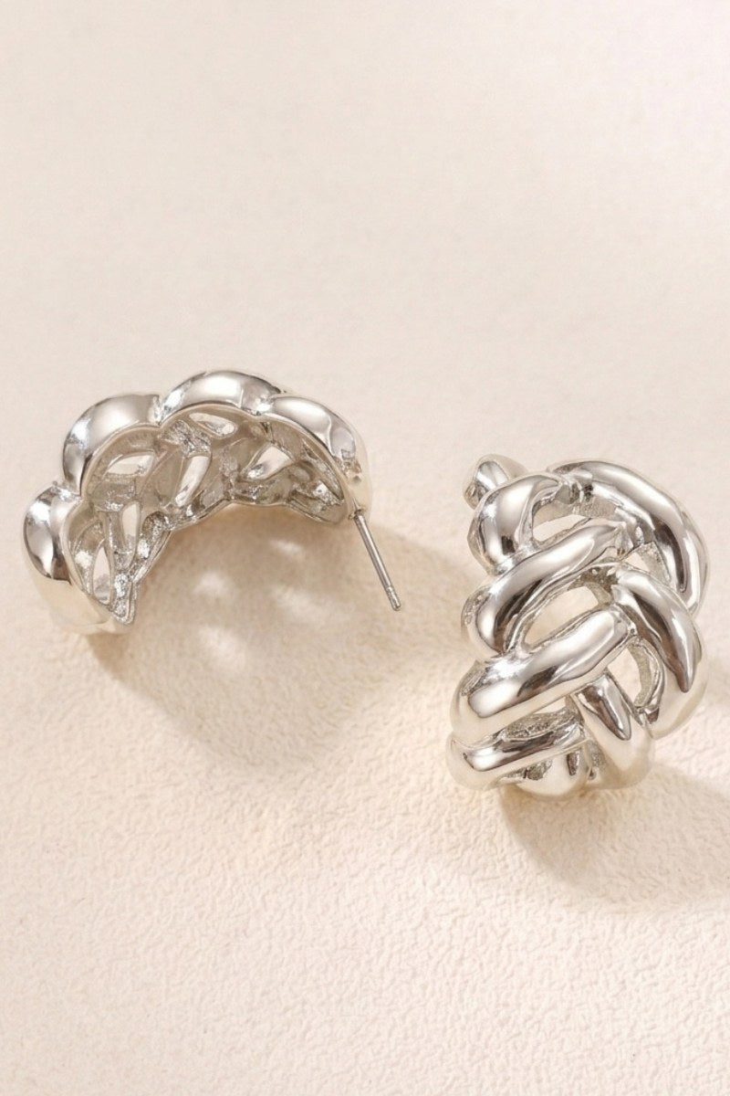 Braided liquid silver half-hoop earrings on a warm beige background