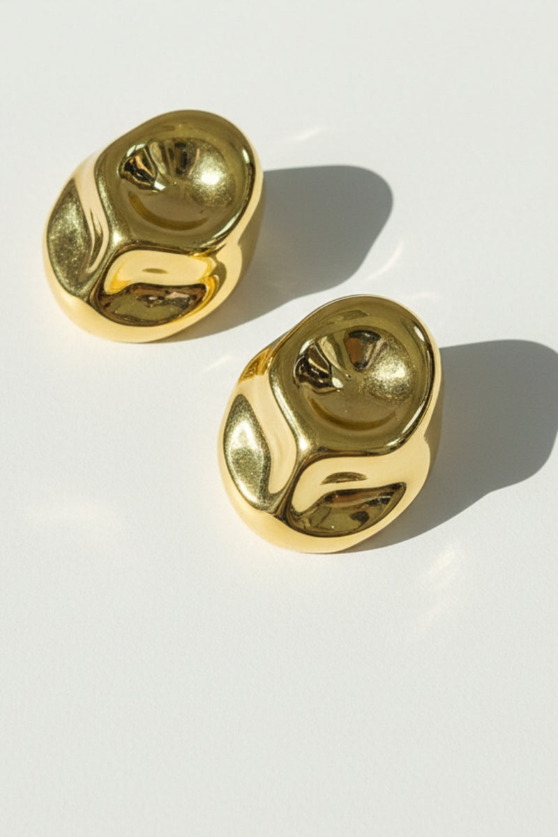 Pair of Isla molten gold statement earrings with a high-shine reflective surface and unique sculptural design on a neutral background.