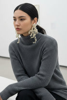 Side view of a sophisticated woman in New York City wearing All Glows fluid pearl drop earrings with a black high-neck sweater.