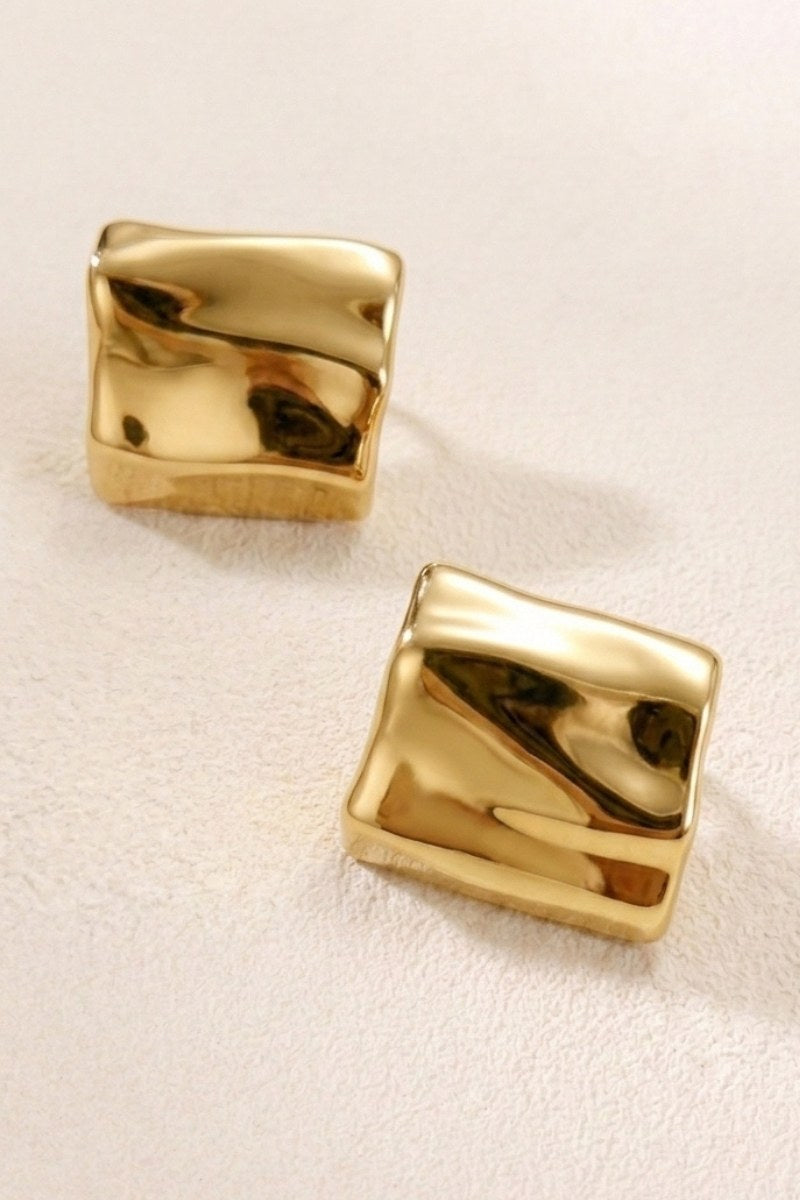 Crinkled gold square statement studs on a warm beige background