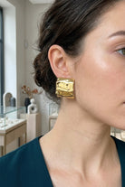 Model wearing crinkled gold square statement studs, view 7