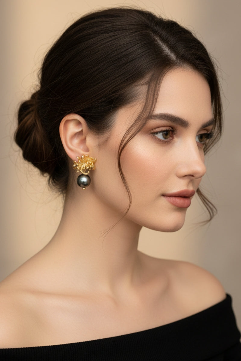 Side profile of a woman with an elegant updo wearing 18K gold-plated sculptural flower earrings with a single black pearl drop, showcasing dark academia aesthetic jewelry for minimalist cocktail styling.