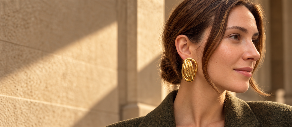 Model wearing sculptural gold oval knot statement earrings in autumn light