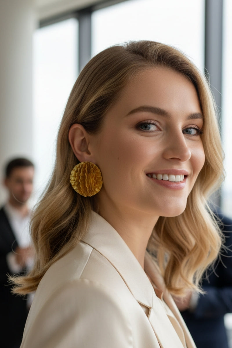 Woman wearing oversized gold honeycomb textured disc earrings in a modern office party setting.