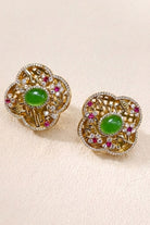 Green crystal quatrefoil stud earrings on a warm beige background