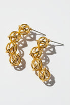 Two hollow gold ball statement studs layout flat under strong daylight, casting dramatic geometric shadows that emphasize the high-shine 18K gold plating and delicate metallic wire craftsmanship.