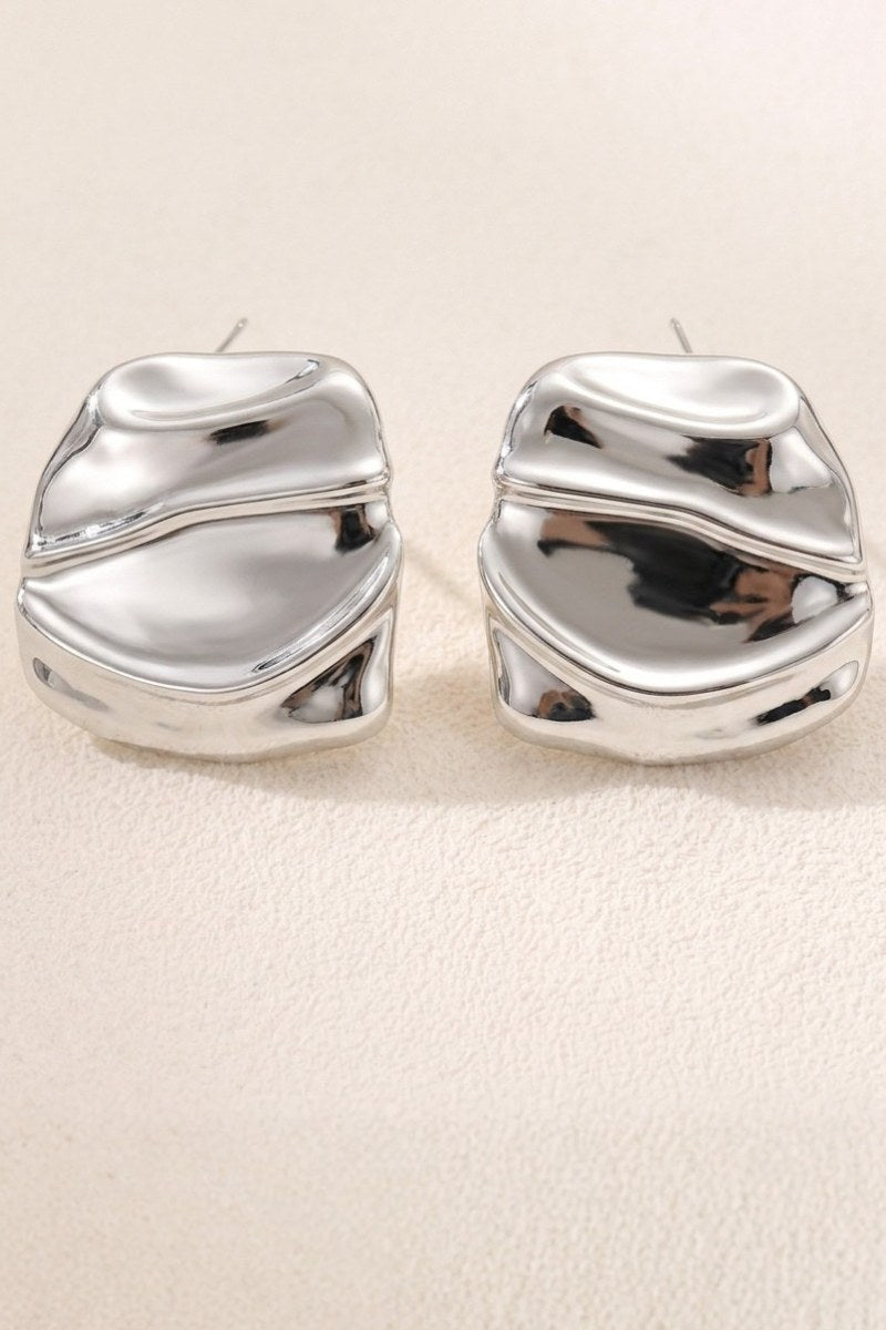 Liquid silver square statement stud earrings on a warm beige background