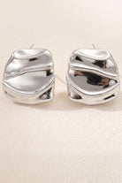Liquid silver square statement stud earrings on a warm beige background