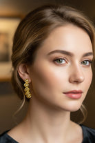 An elegant portrait of a woman with an classic updo wearing a black off-the-shoulder velvet dress, accessorized with luxury gold curved drop earrings that draw focus to her jawline for cocktail attire inspiration.
